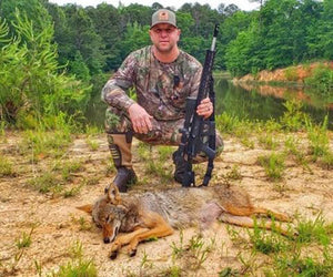 Chad Myers crouches next to a coyote he killed with the rifle he also poses with