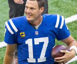 Philip Rivers smiles off to the side in his football uniform, holding a football under his arm