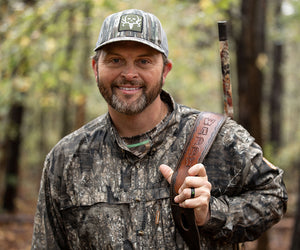 Michael Waddell, dressed in camo, smiles while holding his gun strap
